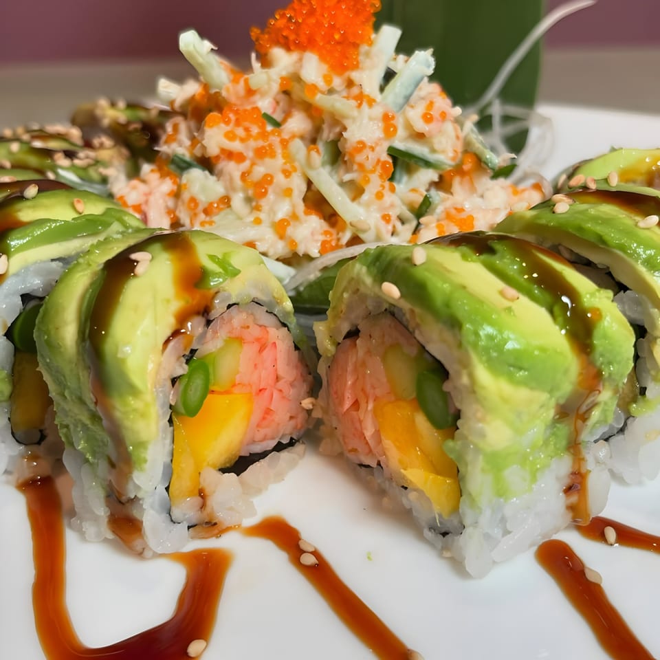 Sushi Guys' avocado-topped sushi rolls with mango and shrimp, drizzled with sauce, alongside a crab salad.