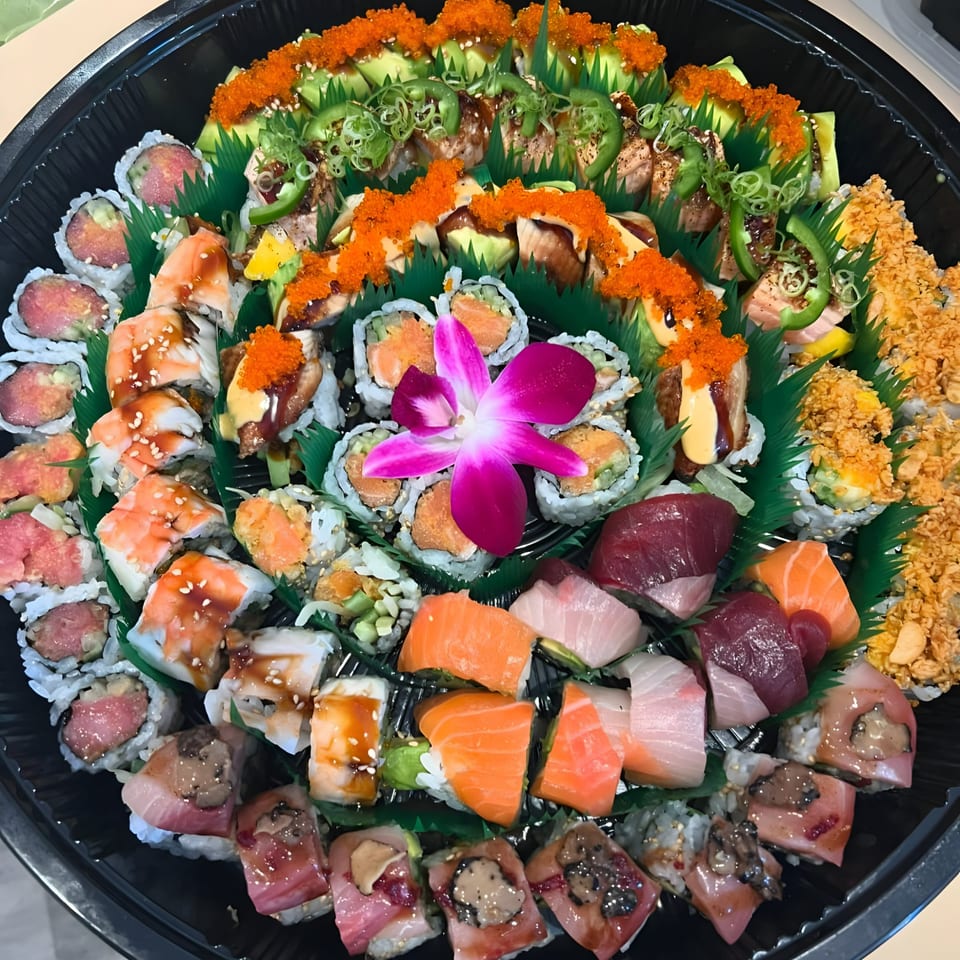 Large platter of assorted Sushi Guys sushi rolls, sashimi, and nigiri, garnished with a purple orchid.