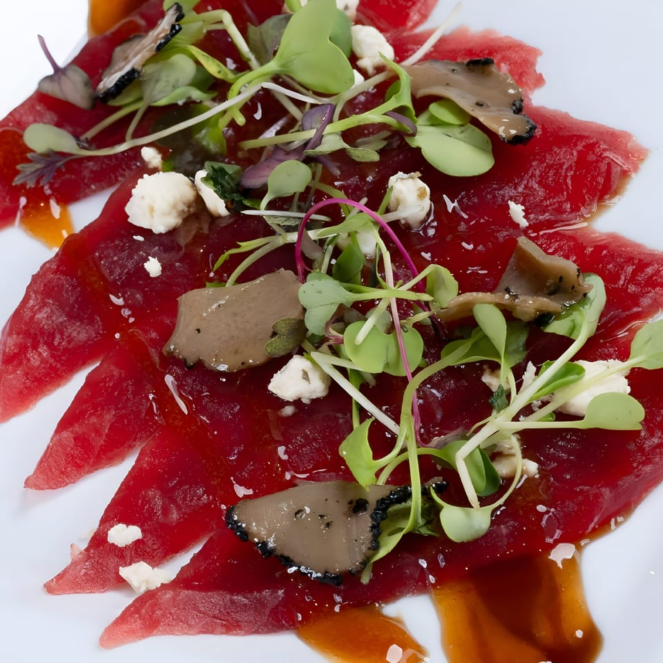 Sushi Guys' tuna sashimi with microgreens, cheese crumbles, and truffle slices on a white plate.