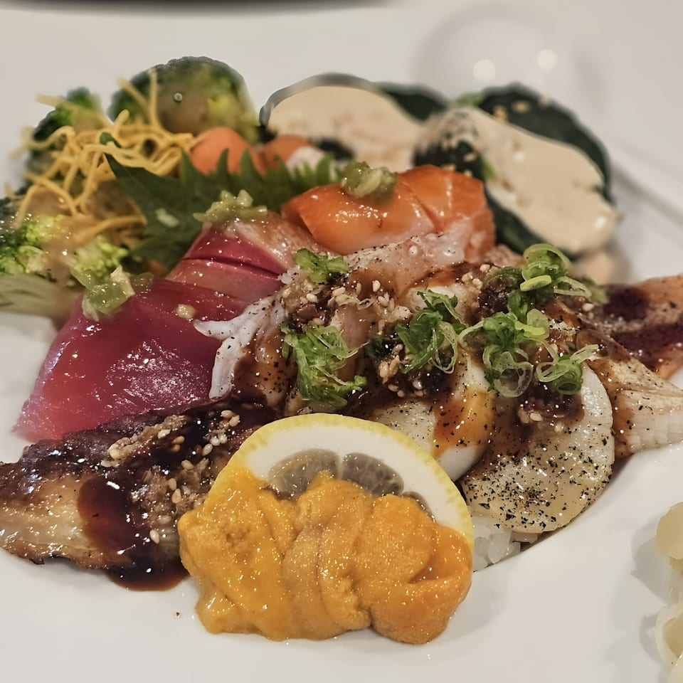 A colorful chirashi bowl from Sushi Guys, featuring various sashimi, uni, and vegetables.